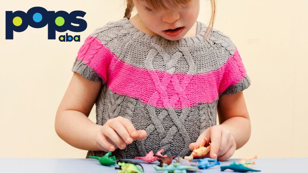 A young girl wearing a brown and pink knitted shirt plays with puzzle pieces, head bowed, focused and fully engaged, illustrating autism support levels.